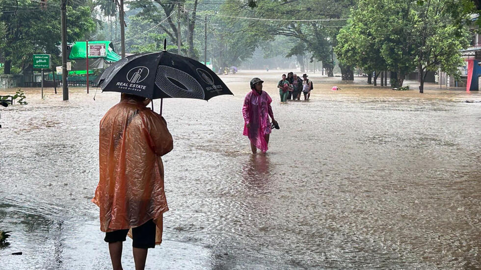 Varias personas caminan por una calle anegada a causa de las abundantes lluvias en Myitkyina, el 2 de julio de 2024 al norte de Birmania