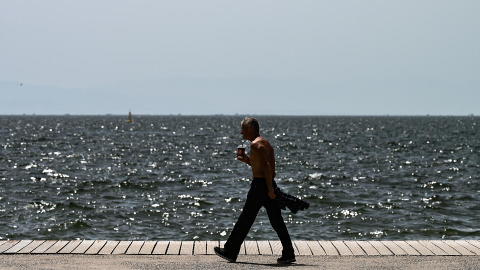 Un hombre camina sin camiseta al borde del mar en la ciudad griega de Salónica el 12 de junio de 2024