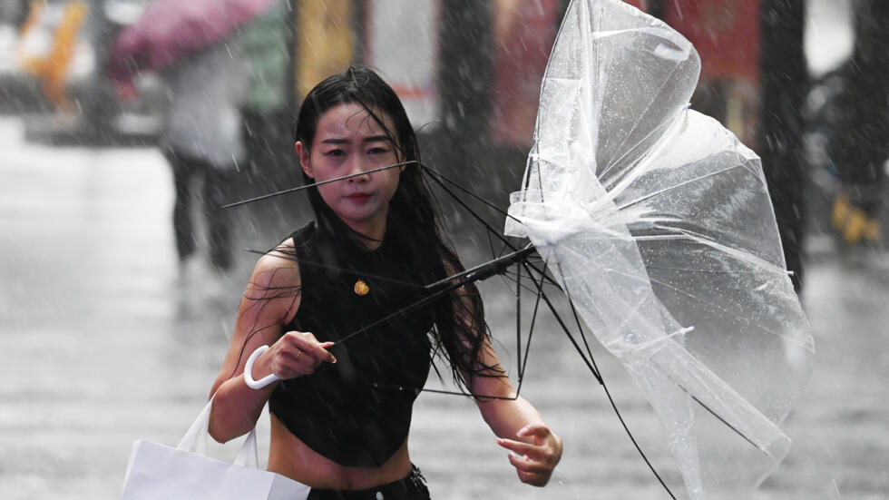 Una joven sostiene un paraguas roto por el viento en medio de un fuerte aguacero, el 31 de julio de 2024 en Pekín