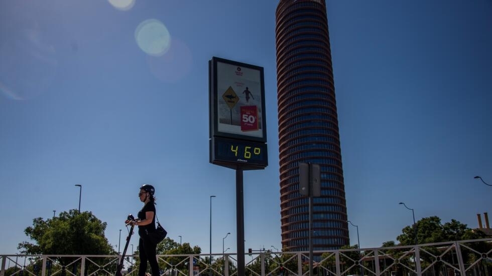Una mujer pasa en patinete ante un termómetro callejero que marca 46 grados centígrados de temperatura, el 23 de julio de 2024 en la ciudad española de Sevilla