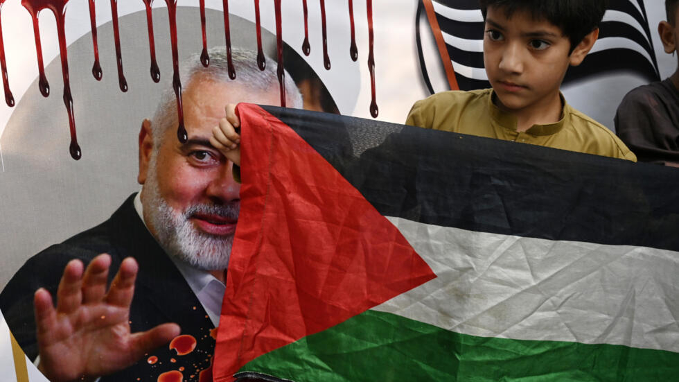 Un niño sostiene una bandera palestina junto a una imagen de Ismail Haniyeh durante una protesta por su asesinato, el 2 de agosto de 2024 en mla ciudad paquistaní de Lahore