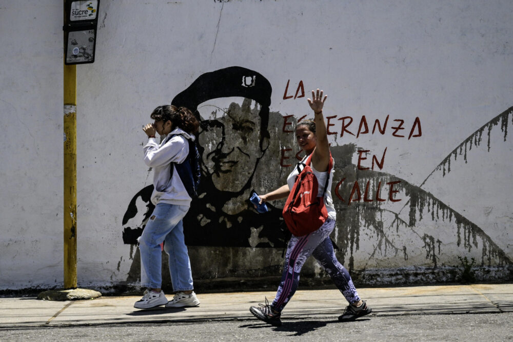 Deux femmes passent devant un graffitti représentant l'ancien président vénézuélien Hugo Chavez, accompagné de la phrase: "L'espoir est dans la rue", dans le bidonville de Petare, dans l'est de Caracas, le 1er août 2024.
