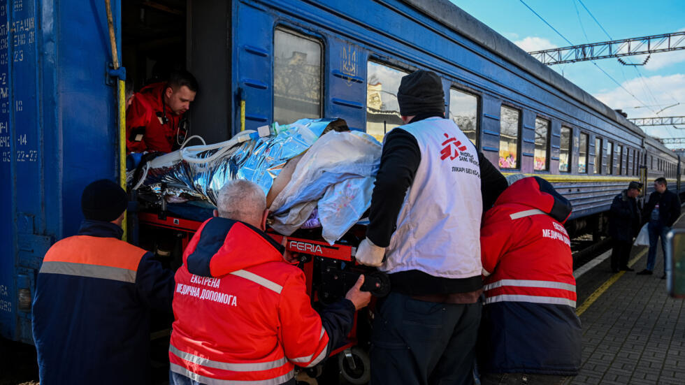 Personal sanitario, ayudado por un miembro de Médicos Sin Fronteras (con chaleco blanco), sacan en camilla de un tren a un civil herido en el este de Ucrania y trasladado para recibir tratamiento, el 17 de marzo de 2023 en Leópolis, al oeste del país