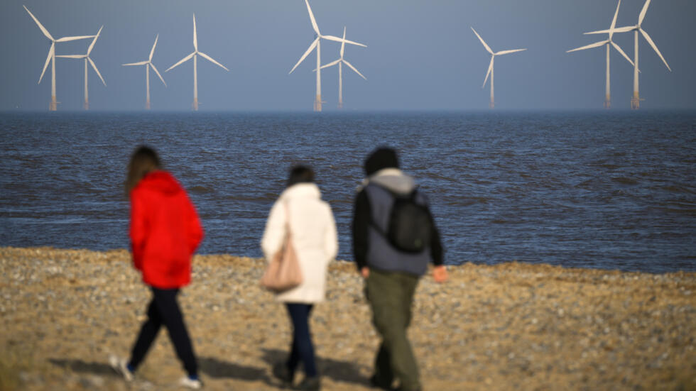 Varias personas caminan por la costa de Great Yarmouth, en el este de Inglaterra, con las turbinas eólicas del proyecto Scroby Sands de fondo, el 15 de febrero de 2023