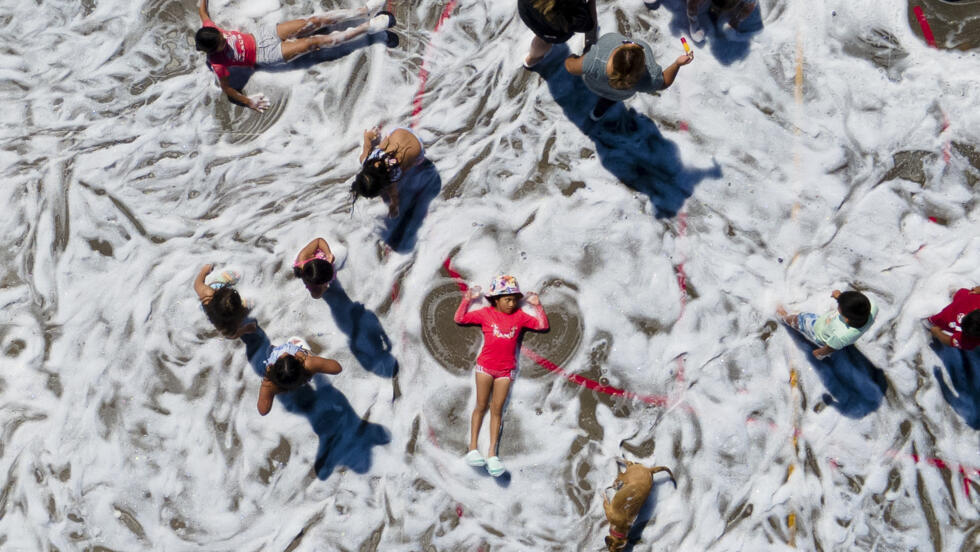 Un niño forma alas de ángel mientras otros niños retozan en una cancha cubierta con espuma de jabón, durante una actividad de verano en Tongoy, Chile, el jueves 25 de enero de 2024. (AP Photo/Matias Basualdo)