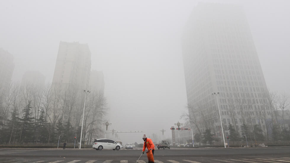 Un empleado de la limpieza trabaja en una calle de Qingzhou mientras la neblina y el aire contaminado envuelven los edificios de esa ciudad al este de China, el 28 de diciembre de 2023