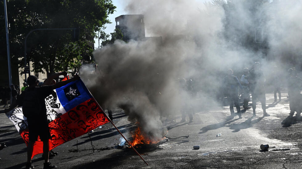 Un manifestante sostiene la bandera de Chile cerca a una barricada durante la marcha por el quinto aniversario del "estallido social", en Santiago, el 18 de octubre de 2024