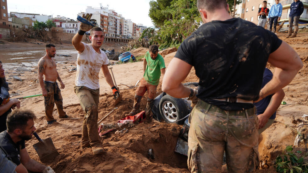 Un grupo de personas trata de desenterrar un automóvil sepultado por el lodo de las inundaciones en busca de posibles víctimas, el 1 de noviembre de 2024 en la localidad española de Paiporta, cerca de Valencia