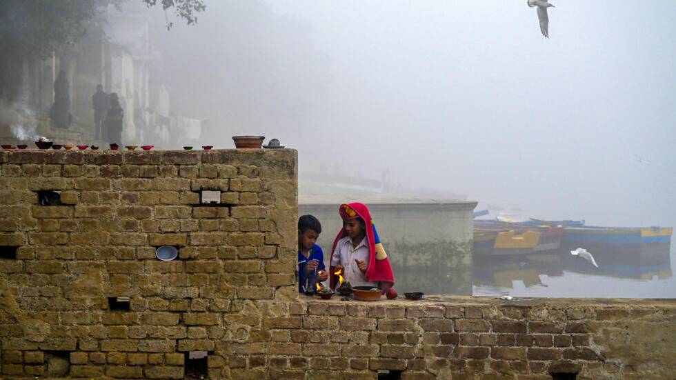 Dos niños encienden lámparas a orillas del río Yamuna, envueltos en smog, el 14 de noviembre de 2024 en Nueva Delhi