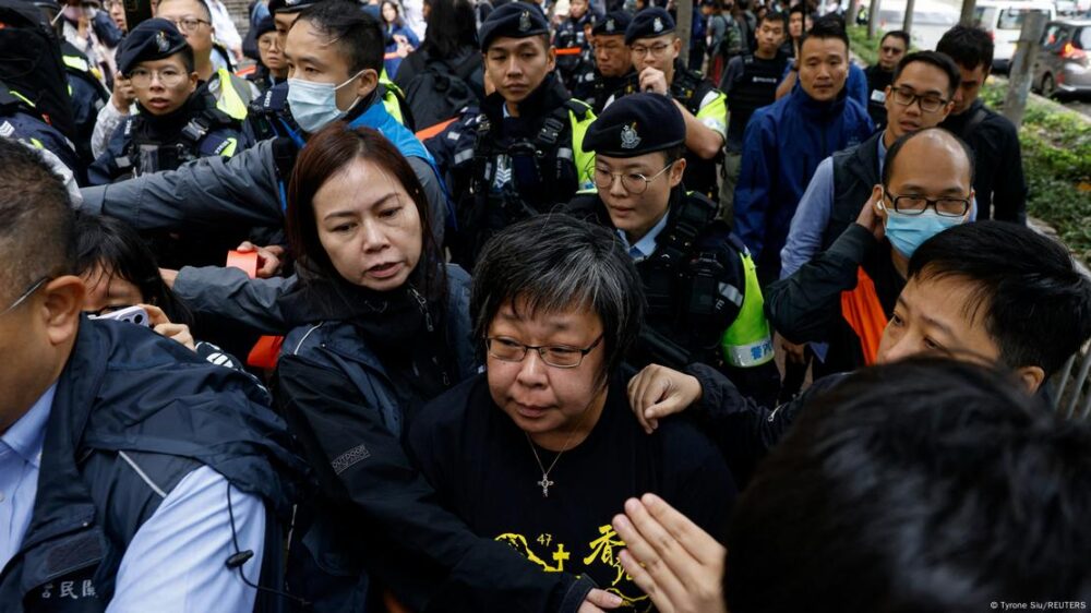 La policía se lleva a una mujer para registrarla en el exterior del Tribunal de Magistrados de West Kowloon, antes de la sentencia contra los 45 activistas prodemocracia condenados en Hong Kong, el martes (19.11.2024)