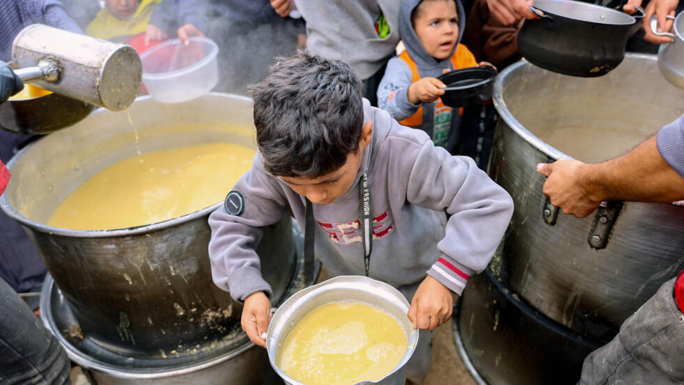 Unos niños palestinos reciben un plato de lentejas en un punto de distribución de alimentos de voluntarios en Gaza el 19 de noviembre de 2024