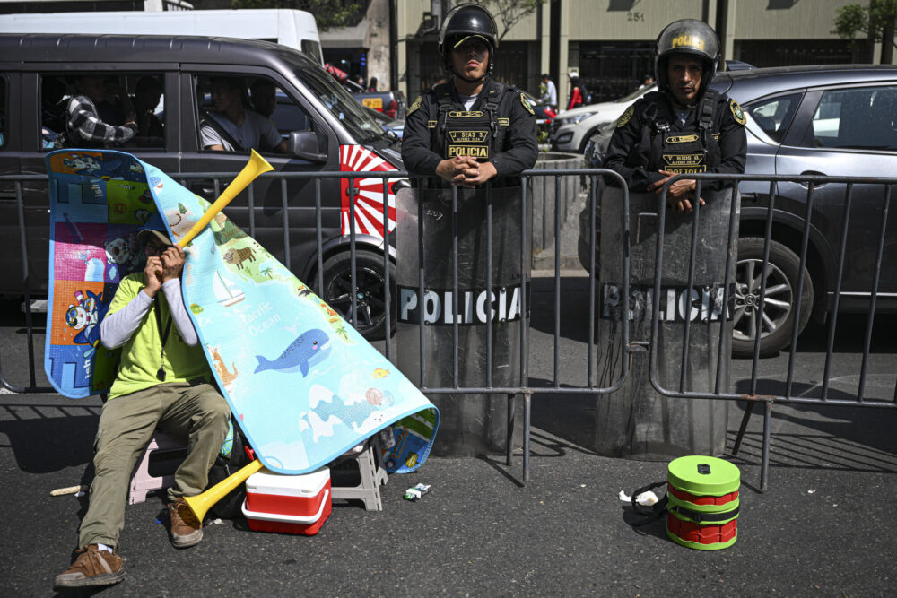 Un minero descansa cerca de policías antimotines en Lima, el 22 de noviembre de 2024, en el marco de protestas frente al Congreso peruano, donde trabajadores de la minería artesanal reclaman extender el plazo para formalizarse, que vence a fin de año