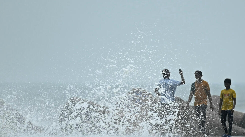 Personas caminan entre el oleaje en un muelle pesquero en Chennai, India, el 27 de noviembre de 2024