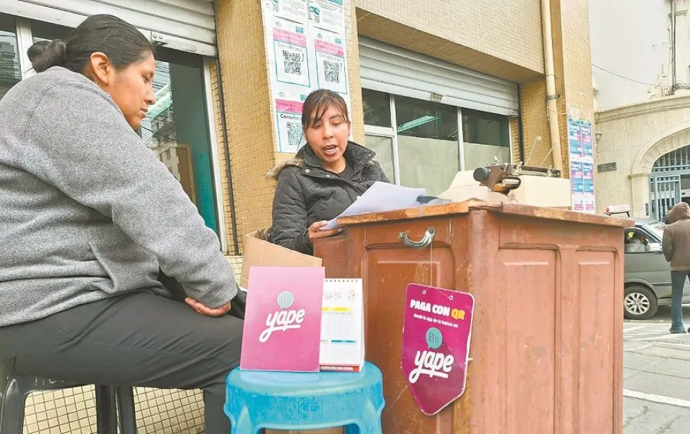 Una persona que ayuda a llenar formularios de pago de impuestos, junto al cartel de Yape en La Paz. Foto: M. Belmonte