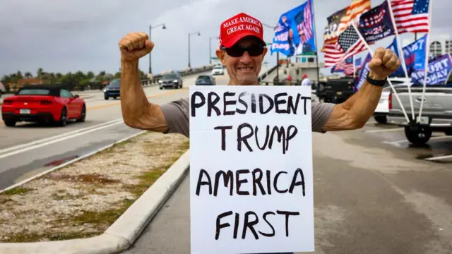 Un hombre sostiene un cartel que dice "Presidente Trump, América primero"