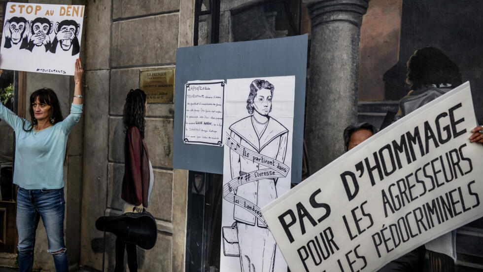 "No a los homenajes a los agresores y los pedocriminales" y "Basta de negación", se lee en las pancartas de dos personas que protestan delante de un fresco que representa al abate Pierre, en Lyon, Francia, el 21 de octubre de 2024