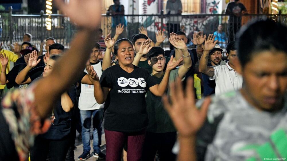 Un grupo de migrantes ora con los brazos extendidos en una plaza de Tapachula.