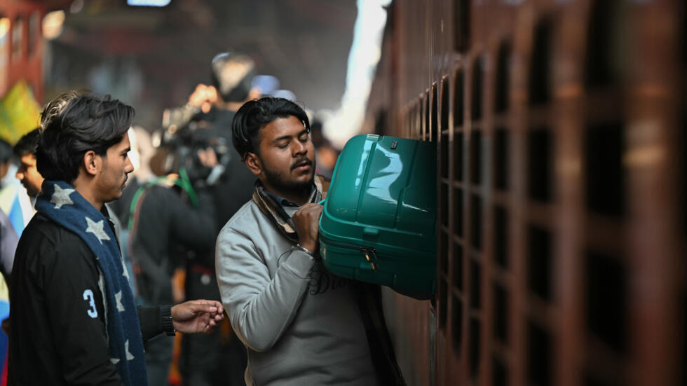 Un pasajero saca su equipaje por la ventanilla de salida de emergencias de un tren el 16 de febrero de 2025 en la estación de Nueva Delhi