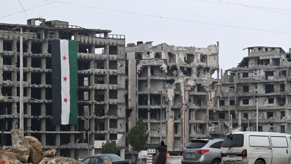 Una mujer mira una bandera de la época de la independencia siria colgada en un edificio destruido en el distrito de Khalidiya, en la ciudad de Homs, el 10 de febrero de 2025