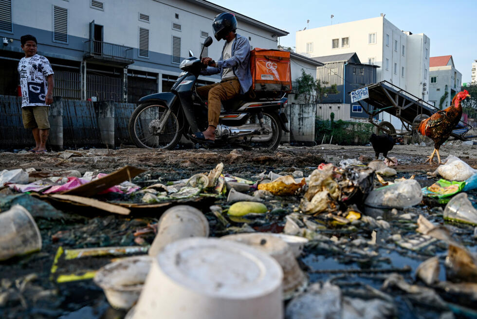 Una motocicleta circula junto a un canal lleno de desechos, en Phnom Penh, el 31 de enero de 2025