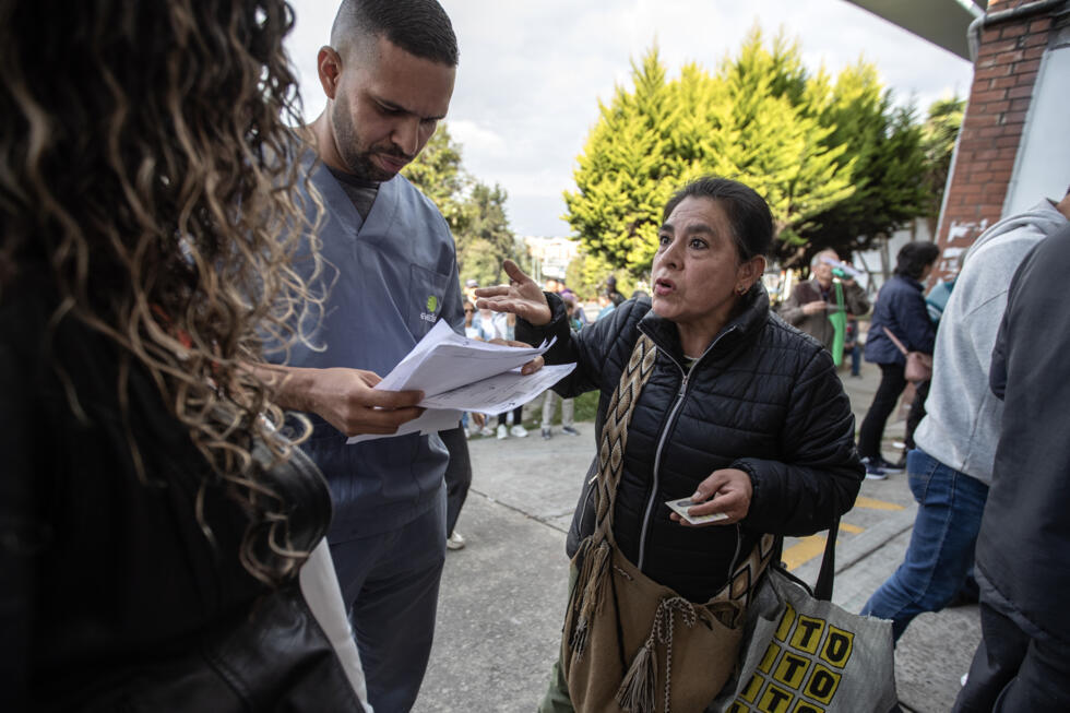 Albenis Muse (derecha) habla con empleados de un dispensario médico mientras hace cola esperando las medicinas de su hermano en Bogotá el 5 de febrero de 2025.