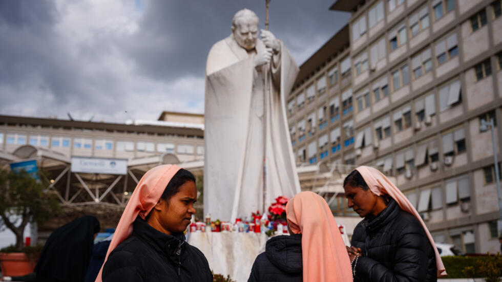 Unas monjas rezan por el papa Francisco ante la estatua del pontífice Juan Pablo II en el exterior del hospital Gemelli de Roma el 27 de febrero de 2025