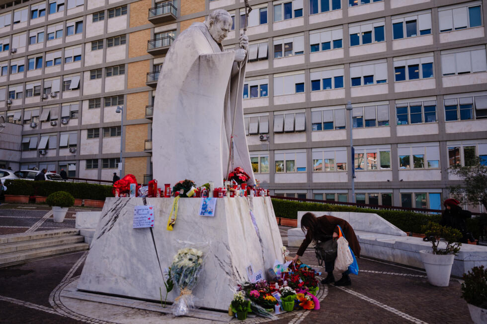 Flores y velas depositadas en la estatua del papa Juan Pablo II en el exterior del hospital Gemelli de Roma, donde el 27 de febrero de 2025 permanece ingresado el pontífice Francisco