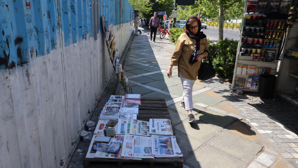Una mujer pasa por un quiosco de prensa de Teherán, con periódicos dedicados a las conversaciones en Roma entre Irán y EEUU sobre el programa nuclear, el 19 de abril de 2025