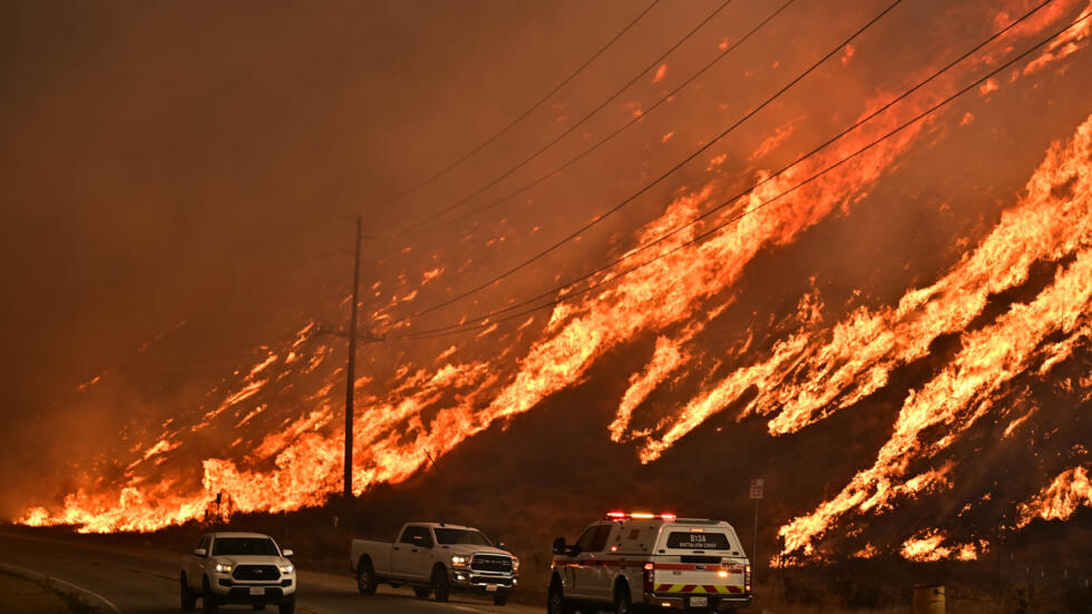 Carros de emergencias se movilizan por un costado de una ruta frente a llamas del Incendio Hughes que suben la colina en Castaic, un barrio del noroeste de Los Angeles, California, el 22 de enero de 2025