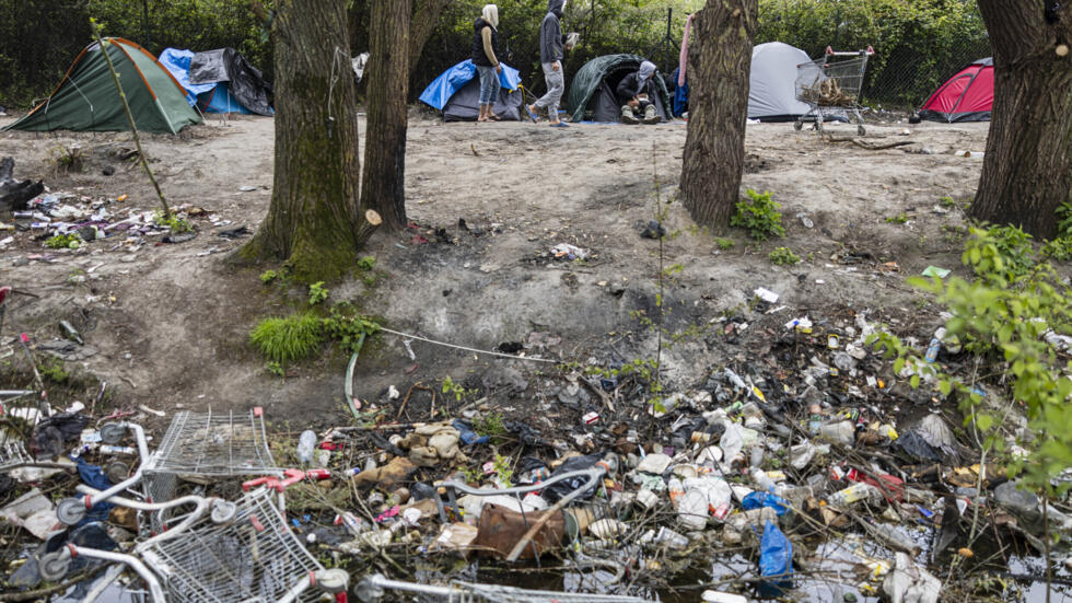 Unos migrantes caminan junto a unas tiendas del campamento de Loon-Plage, en el norte de Francia, el 25 de abril de 2024