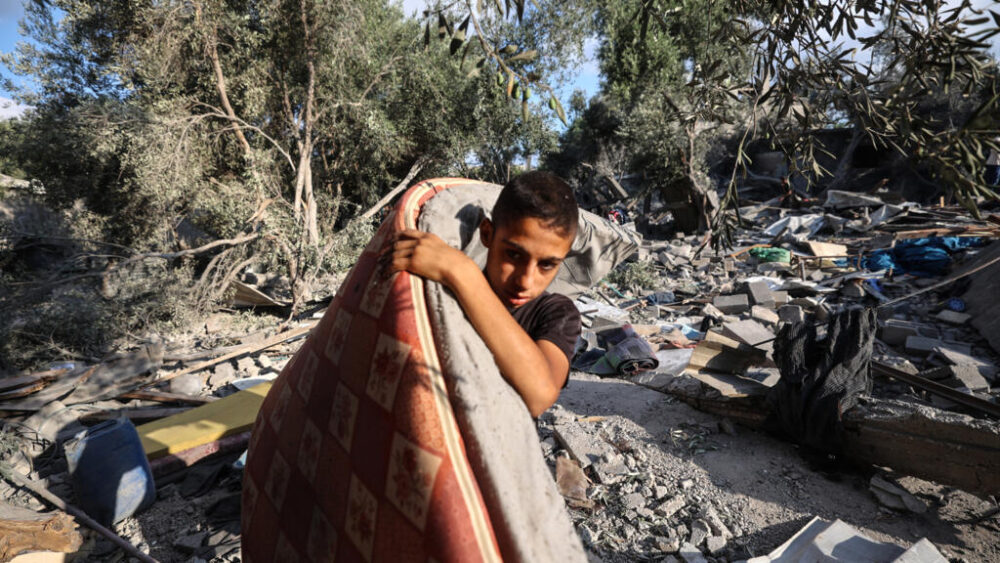Un chico palestino recoge un colchón de los escombros de una casa, tras un bombardeo israelí en Nuseirat el 13 de julio de 2025