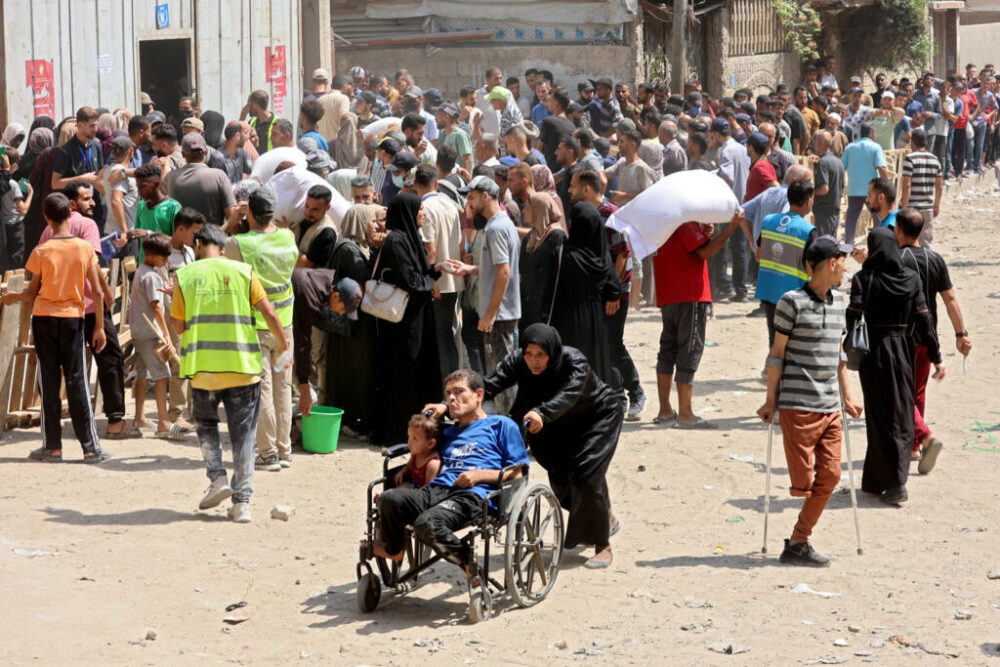 Una mujer palestina empuja a un hombre y un niño en silla de ruedas, cerca de un centro de recogida de harina en un depósito del Programa Mundial de Alimentos en Ciudad de Gaza, el 12 de julio de 2025