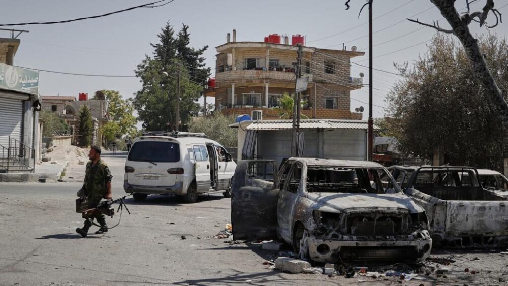 Un miliciano druso armado con una ametralladora pasa junto a un coche calcinado tras los enfrentamientos sectarios que tuvieron lugar la semana pasada en la ciudad de Suwayda, de mayoría drusa, en Siria, el 25 de julio de 2025.