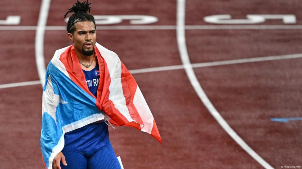 El deportista, todavía en la pista, envuelto en la bandera de Puerto Rico.