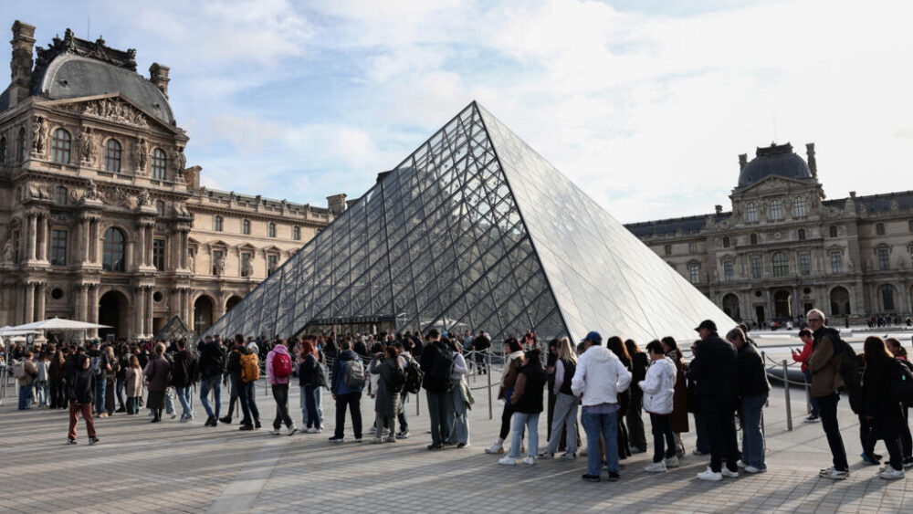 Los visitantes hacen fila junto a la conocida pirámide de cristal para entrar en el museo del Louvre, el 22 de octubre de 2025 en París, tres días después del robo de las joyas