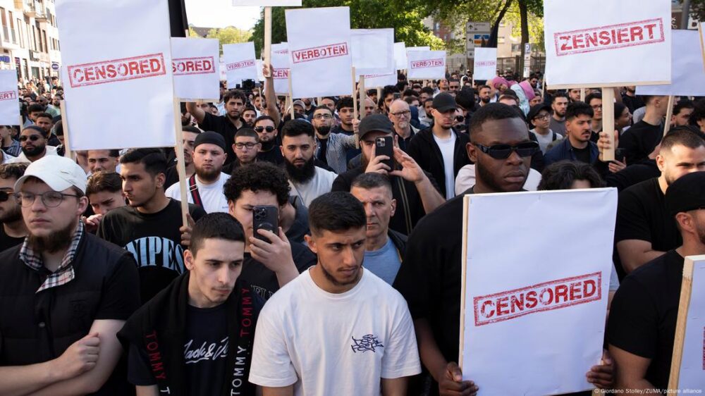 Una multitud de hombres con camisetas negras o blancas, sostienen pancartas con la palabra 'censurado' en inglés.