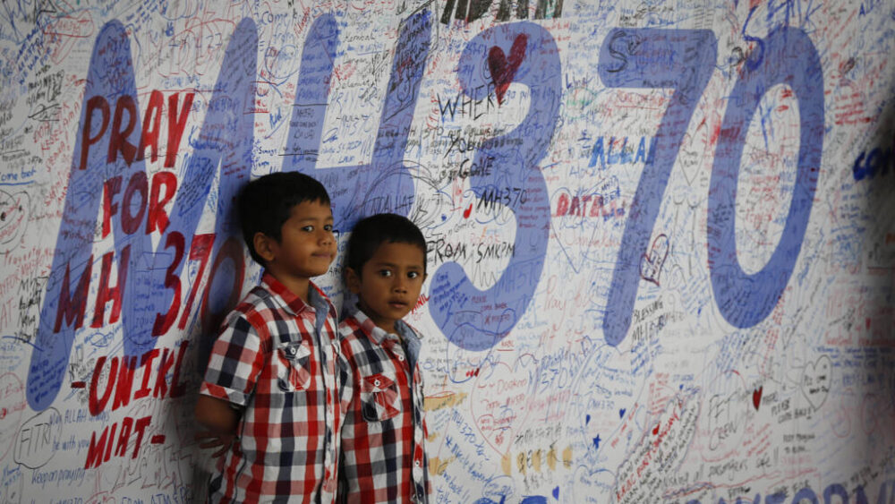 ARCHIVO - Dos niños malayos frente a un tablón de mensajes y buenos deseos para las personas relacionadas con el avión desaparecido MH370 de Malaysia Airlines, en Sepang, Malasia, el 16 de marzo de 2014. Hace diez años, el vuelo 370 de Malaysia Airlines desapareció el 8 de marzo de 2014 cuando cubría la ruta entre Kuala Lumpur y Pekín con más de 200 personas a bordo. 