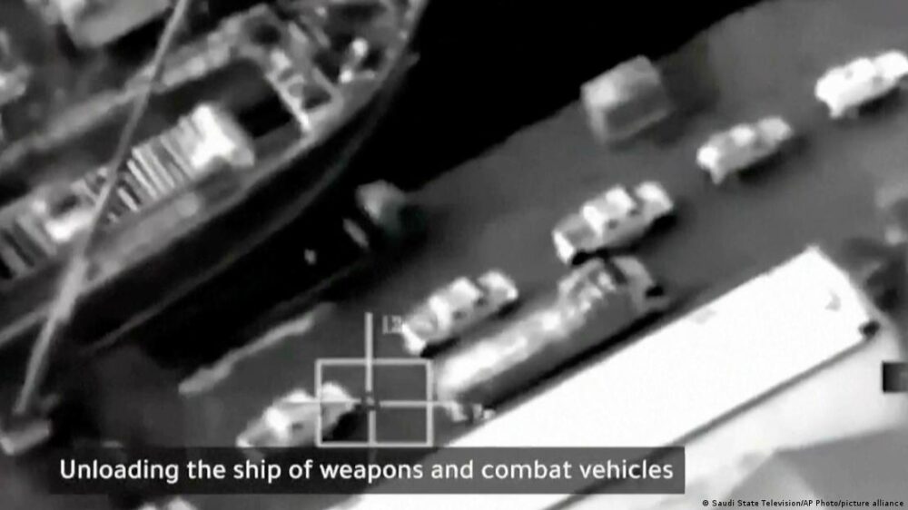 La imagen aérea muestra un camión y vehículos tipo pick-up en el muelle junto a un barco. La imagen aérea muestra un camión y vehículos tipo pick-up en el muelle junto a un barco.