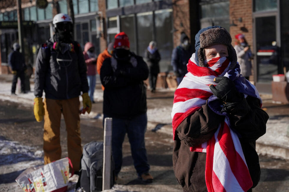 Una persona envuelta en una manta con el color de la bandera de Estados Unidos se encuentra cerca del lugar donde agentes federales dispararon fatalmente a un hombre identificado como Alex Pretti mientras intentaban detenerlo, en Minneapolis, Minnesota, Estados Unidos, el 24 de enero de 2026.