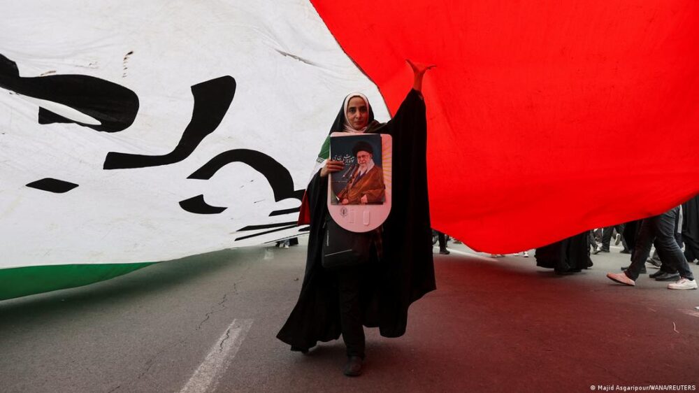 Irán Teherán 2026 | Mujer bajo una bandera gigante, con cartel del ayatolá Alí Jamenei, en la celebración del 47 aniversario de la Revolución Islámica. Irán Teherán 2026 | Mujer bajo una bandera gigante, con cartel del ayatolá Alí Jamenei, en la celebración del 47 aniversario de la Revolución Islámica.