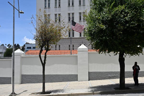 Una bandera estadounidense ondea detrás de una alta valla blanca con un edificio de oficinas detrás.