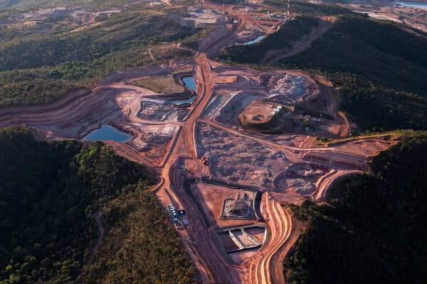 Una amplia toma aérea muestra una gran explotación minera, con extensos movimientos de tierra de color marrón rojizo y carreteras serpenteantes.