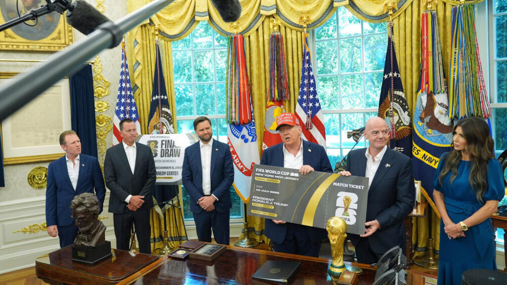 El presidente Donald Trump habla sosteniendo una entrada grande que representa una entrada para la final de la Copa del Mundo, fila uno, asiento uno, mientras Andrew Giuliani, de izquierda a derecha, Richard Grenell, presidente de la Junta Directiva del Centro Kennedy, el vicepresidente JD Vance, el presidente de la FIFA Gianni Infantino y la secretaria de Seguridad Nacional Kristi Noem escuchan en el Despacho Oval de la Casa Blanca, el 22 de agosto de 2025, en Washington.