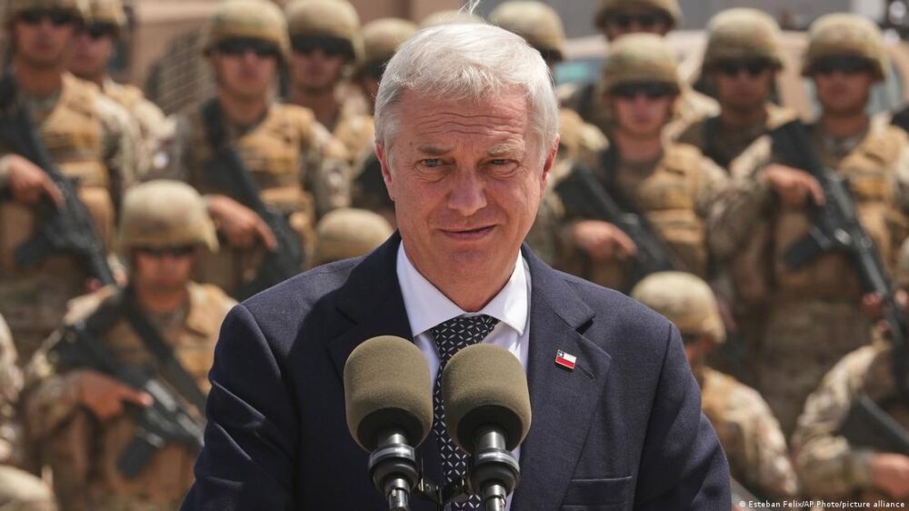 José Antonio Kast mira hacia la cámara mientras de fondo, desenfocados, se ven soldados del Ejército de Chile. José Antonio Kast mira hacia la cámara mientras de fondo, desenfocados, se ven soldados del Ejército de Chile.