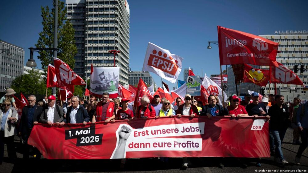 Una multitud con banderastras una pancarta en la que se lee "1º de Mayo, primero nuestros trabajos, después vuestros beneficios". Una multitud con banderastras una pancarta en la que se lee "1º de Mayo, primero nuestros trabajos, después vuestros beneficios".