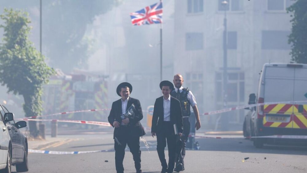 Dos habitantes del barrio de Golders Green pasan frente a una zona, envuelta en humo, acordonada por la policía tras el incendio en un supermercado, el 27 de mayo de 2026 al norte de Londres